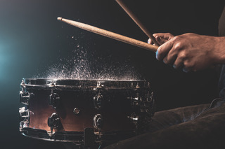 A man plays with drumsticks on a snare drum with splashing water.